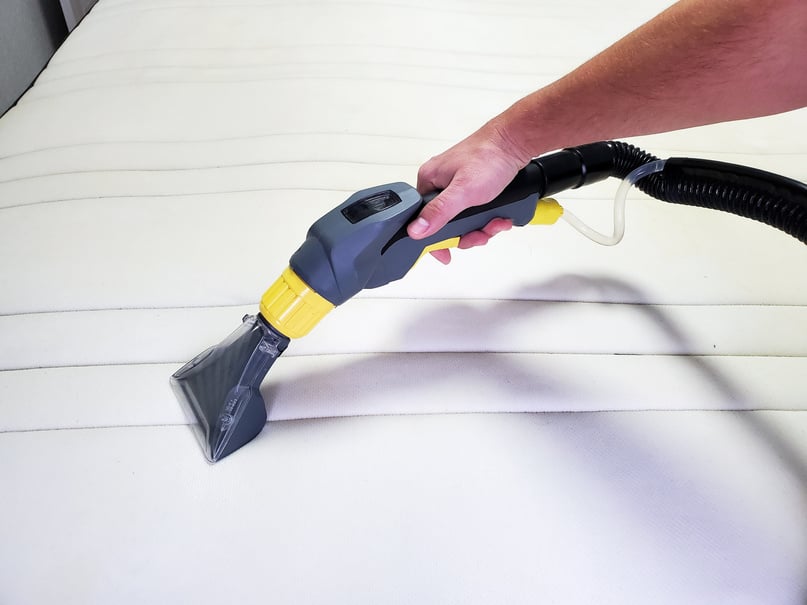 man's hand cleans a modern white mattress with a professional cleaning agent